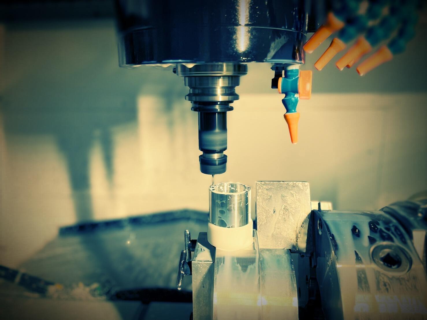 A close-up shot of a CNC milling machine's cutting tool drilling into a cylindrical metal workpiece.