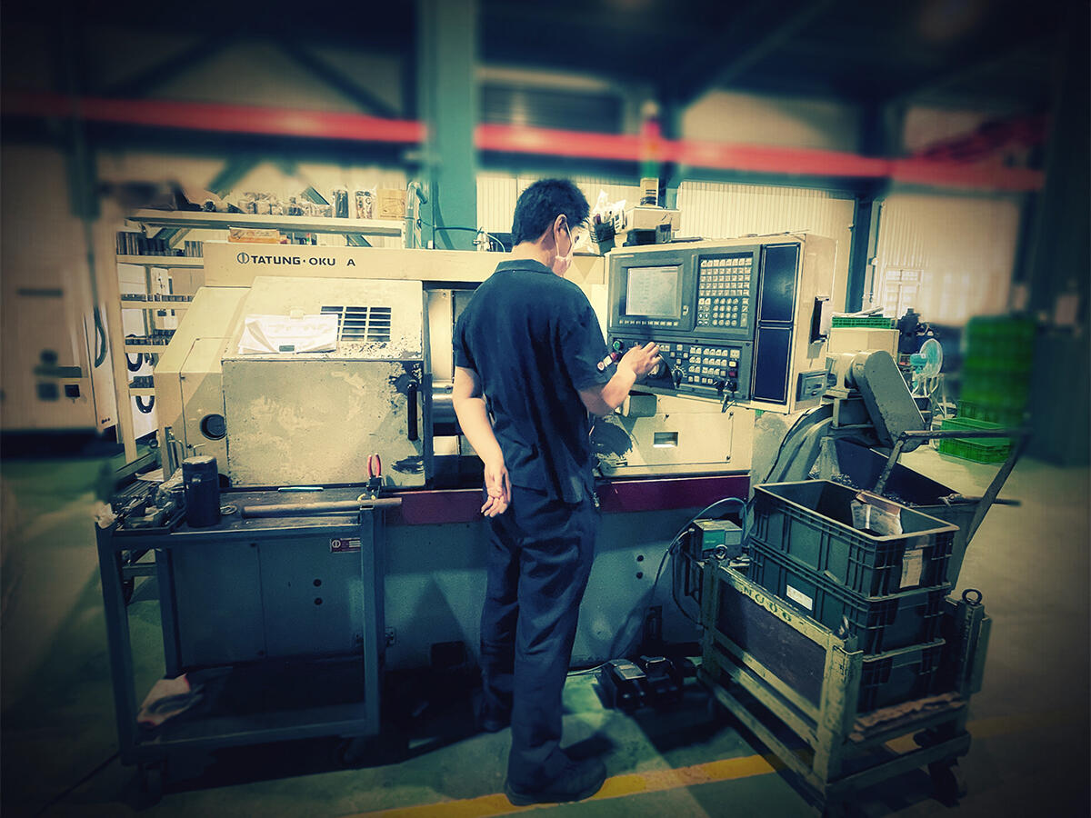 A worker, viewed from behind, operates a large industrial CNC lathe machine.