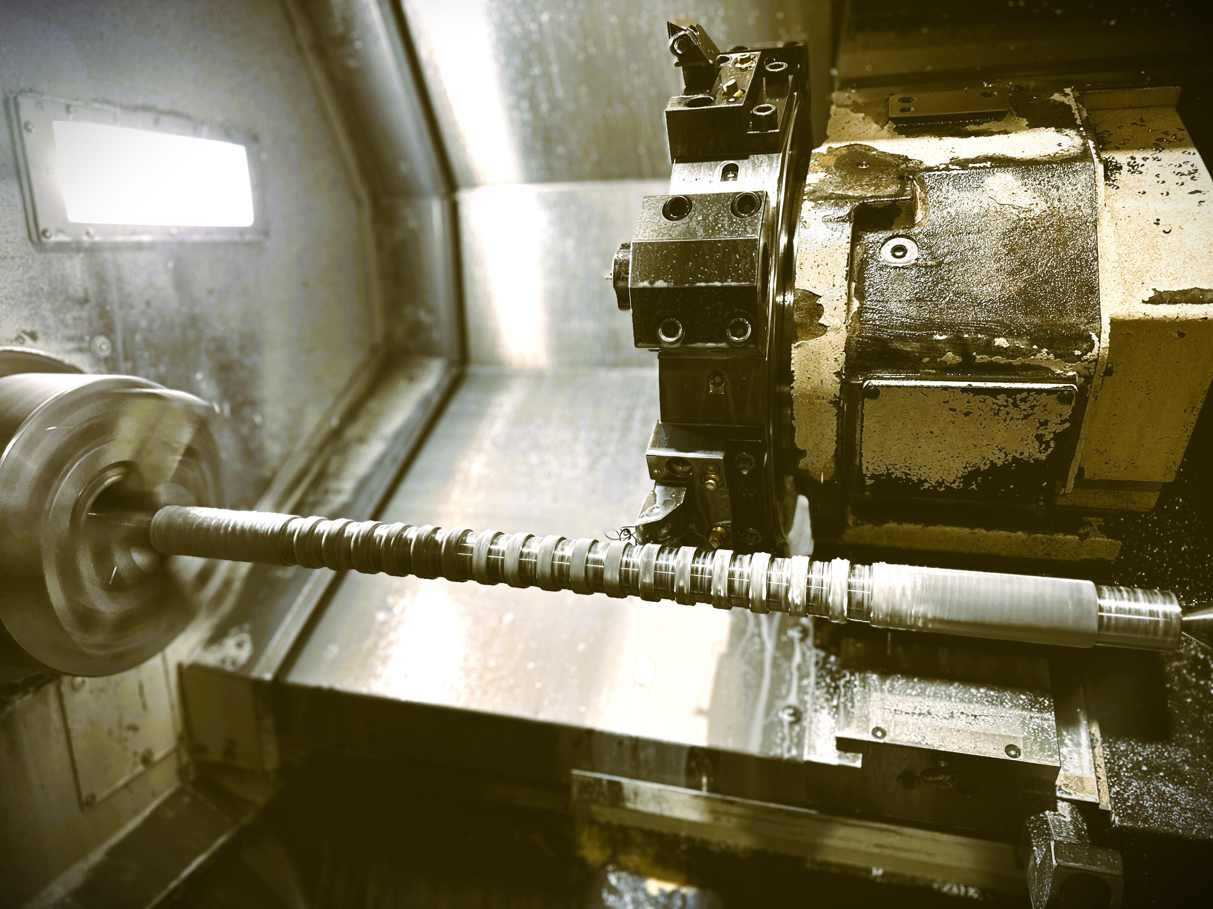 A close-up shot of a CNC lathe machine in the process of shaping a long, cylindrical metal workpiece.